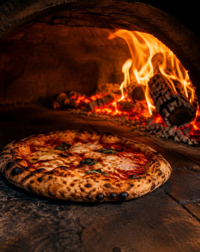 Pizza baking beside a glowing oven fire